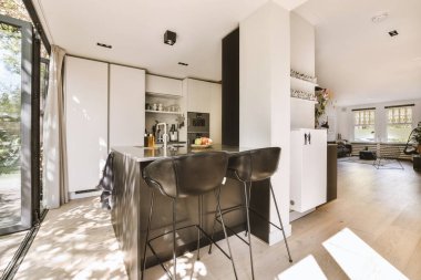 Gündüz vakti çağdaş dairede balkon kapıları olan siyah mutfak ve yemek odası.