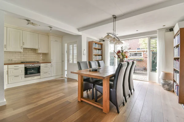 Modern minimalist style interior design of studio apartment with open white kitchen and dining zone with table and chairs illuminated by loft style lamp