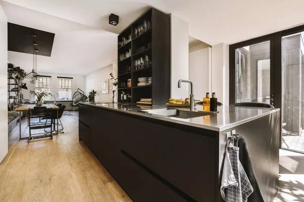 Interior of black kitchen and dining room with balcony doors in contemporary apartment at daytime