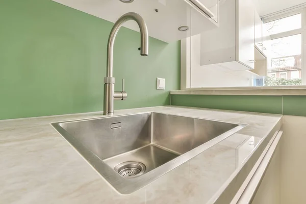 Sink with shiny tap installed under modern counter near jar with spices and gas stove in kitchen at home