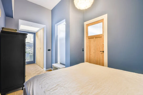 Minimalist interior design of small bedroom with soft bed placed in corner and wooden wardrobe and shelves with lamp illumination