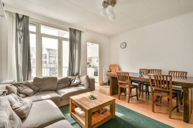 Sandalyeleri ve vazosu olan eski püskü ahşap masa modern apartmanda dekorasyonlu aydınlık duvarlara karşı rahat kanepenin yanında.