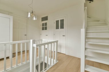 Kapalı beyaz oda kapısı çerçeveli resimlerin yanında ve evdeki merdivenin tepesinde şık bir lamba var.