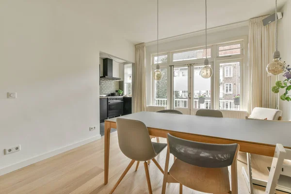 Modern minimalist style interior design of studio apartment with open white kitchen and dining zone with table and chairs illuminated by loft style lamp