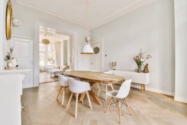 Wooden table with vase of flowers under black pendant lamp in modern living room with armchair near window