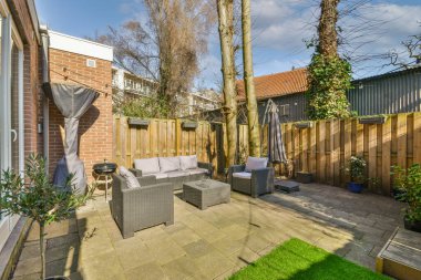 Neat paved patio with sitting area and small garden near wooden fence