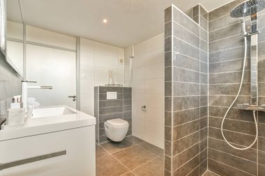 Çağdaş dairenin küçük fayanslı banyosunda lavabo ve duş arasında bulunan sifon tuvaleti