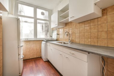 İyi organize edilmiş küçük bir ev mutfağı pencerenin altında lavabo, sobalı hafif mobilyalar ve kentsel apartmanda buzdolabı var.