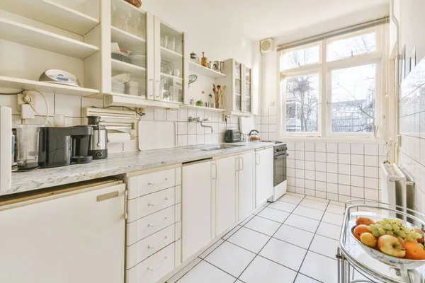 シンクとストーブ付きのミニマリストスタイルの白い家具と光の狭い家庭用キッチンの内部の断片 — ストック写真