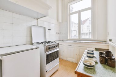 İyi organize edilmiş küçük bir ev mutfağı pencerenin altında lavabo, sobalı hafif mobilyalar ve kentsel apartmanda buzdolabı var.