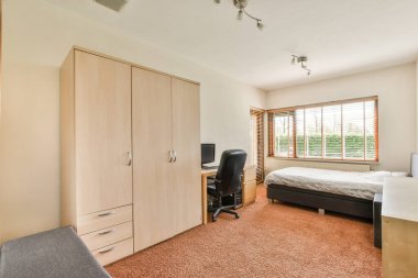 Parlayan lambanın yanında rahat bir yatak ve küçük pencereli çağdaş yatak odasında çerçeveli resimler.