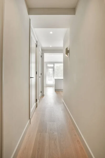 Light narrow hallway with many doors in white walls and glowing lamp over lumber floor