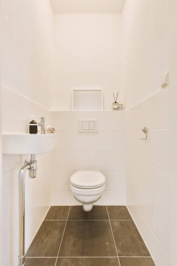 Modern sifon tuvaleti ve seramik lavabo aynanın yanındaki beyaz fayanslı duvarlara ve evdeki küçük tuvaletteki havluya monte edildi.