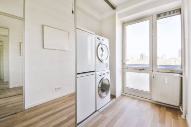 Beyaz duvarları ve koyu renk döşemeleri olan modern, parlak çamaşır odasının içi.