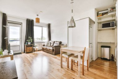 Günümüz minimalist tasarımı. Hafif stüdyo dairesinin ahşap masası ve oturma odası ile beyaz duvarları ve parke zemini arasında yemek masası ve sandalyeleri var.