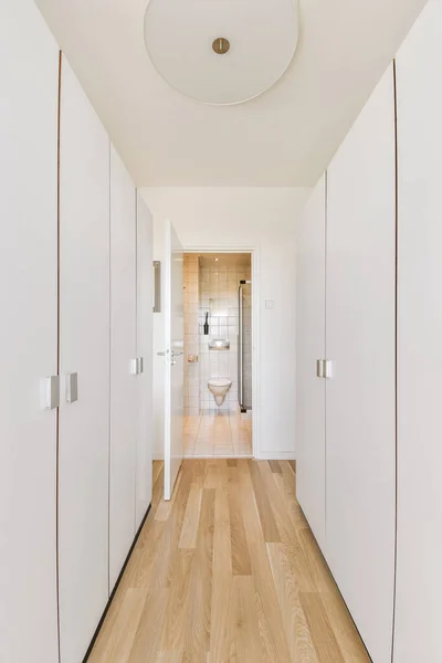 Light narrow hallway with many doors in white walls and glowing lamp over lumber floor