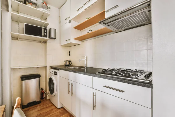 Well organized small home kitchen interior with sink under window and light furniture with stove and fridge in urban apartment