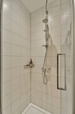 Evdeki modern tuvalette asılı duran banyo musluğu ile duvar arasındaki cam bölme.