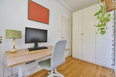 Modern apartmandaki hafif iş yerinde bilgisayar monitörleri ve beyaz tahtanın olduğu masanın yanına konforlu sandalye