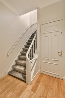 Minimalist iç tasarımı olan modern lüks dairenin ikinci katına çıkan ahşap merdivenli beyaz koridor.