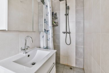 Modern banyoda aynalı lavabo ve cam kapılı duş kutusu ve beyaz fayanslı duvarlar.