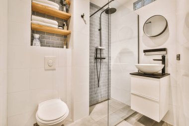 Çağdaş dairenin küçük fayanslı banyosunda lavabo ve duş arasında bulunan sifon tuvaleti