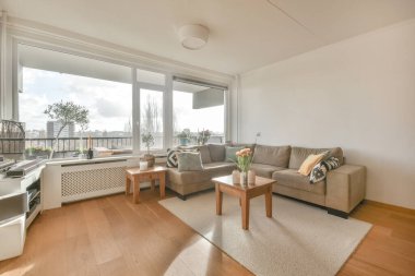 Çağdaş bir dairede pencerelere karşı şık mobilyaları olan geniş bir odanın içinde.