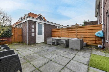 Oturma alanı ve ahşap çitlerin yanındaki küçük bahçesi olan düzgün asfaltlı bir avlu.