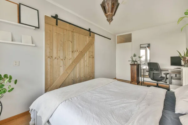 Bed with colorful pillows and blanket located near glass wall of restroom in modern apartment