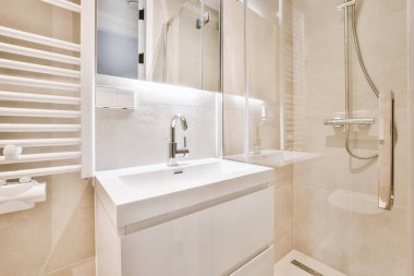 Evdeki çağdaş tuvaletteki aynanın altındaki duvarda musluk ve sıvı sabun asılı.