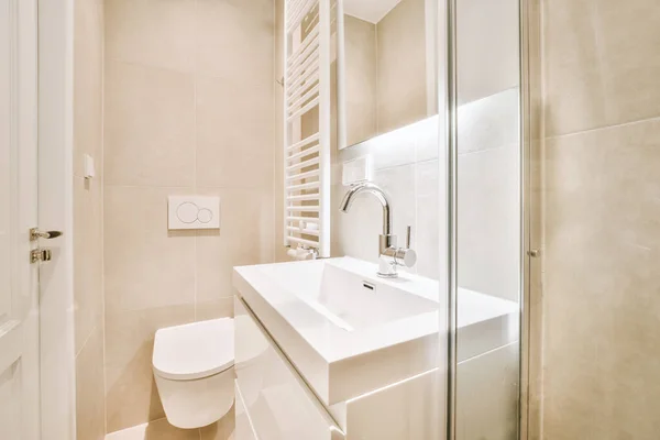 鏡とタオルの近くの白いタイル張りの壁に設置された現代のフラッシュトイレとセラミックシンク自宅の小さなトイレに — ストック写真