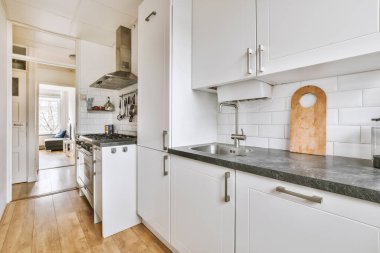 Geniş pencereli hafif küçük ev mutfağı modern kentsel dairede dolaplar ve raflarla donatılmış.