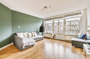 Geniş pencereli, ahşap kanepeli, dolaplı ve televizyonlu modern minimalist oturma odasının iç tasarımı beyaz duvara yerleştirilmiş.