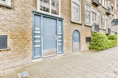 Tabelaları, arabaları, kaldırımları ve ahşap kapıları olan tuğla binanın önü daireye çıkıyor.