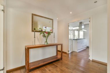 Beyaz oturma odasında açık siyah mutfak, yemek masası ve gri kanepe.