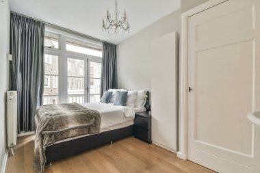 Modern apartmandaki cam tuvalet duvarının yanında renkli yastıklar ve battaniyeli bir yatak.