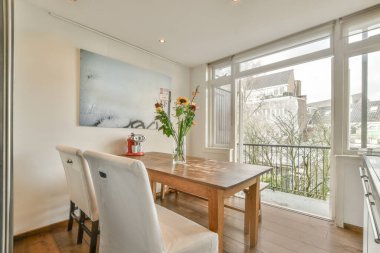 Beyaz oturma odasında açık siyah mutfak, yemek masası ve gri kanepe.