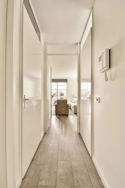 Light narrow hallway with many doors in white walls and glowing lamp over lumber floor