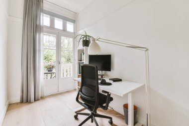 Modern apartmandaki hafif iş yerinde bilgisayar monitörleri ve beyaz tahtanın olduğu masanın yanına konforlu sandalye