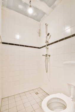 Interior of narrow restroom with shower and wall hung toilet with white walls and checkered floor