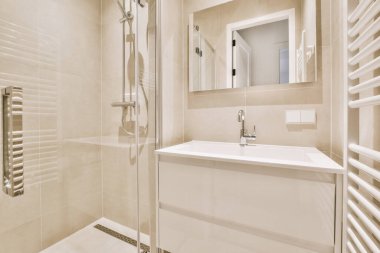 Modern banyoda aynalı lavabo ve cam kapılı duş kutusu ve beyaz fayanslı duvarlar.