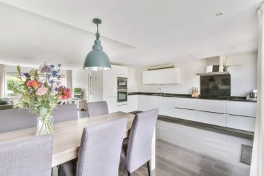 Günümüz minimalist tasarımı. Hafif stüdyo dairesinin ahşap masası ve oturma odası ile beyaz duvarları ve parke zemini arasında yemek masası ve sandalyeleri var.