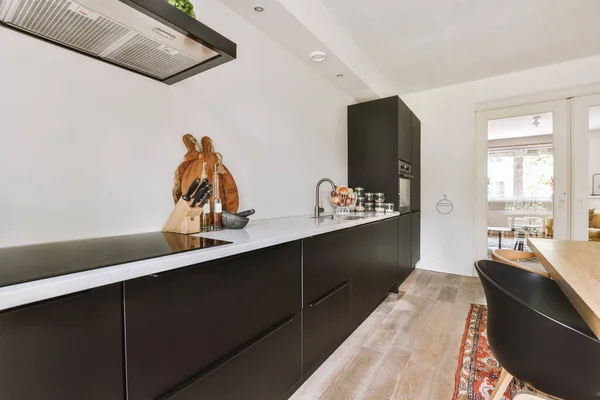 Modern minimalist style interior design of studio apartment with open white kitchen and dining zone with table and chairs illuminated by loft style lamp