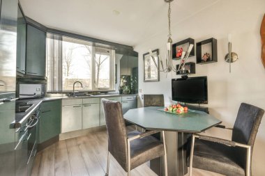 Stüdyo dairesinin modern minimalist tarzı iç tasarımı açık beyaz mutfak ve yemek masası ve sandalyeleri tavan arası lambasıyla aydınlatılmış.