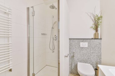 Çağdaş dairenin küçük fayanslı banyosunda lavabo ve duş arasında bulunan sifon tuvaleti