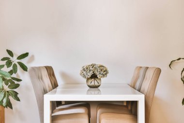 Stüdyo dairesinin modern minimalist tarzı iç tasarımı açık beyaz mutfak ve yemek masası ve sandalyeleri tavan arası lambasıyla aydınlatılmış.