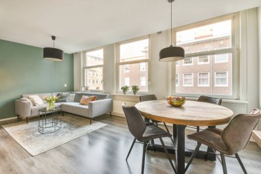 Çağdaş dairenin geniş odasındaki dinlenme odası ve mutfağın yakınındaki sandalyeli ve çiçekli masa.