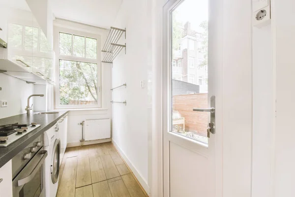 Well organized small home kitchen interior with sink under window and light furniture with stove and fridge in urban apartment