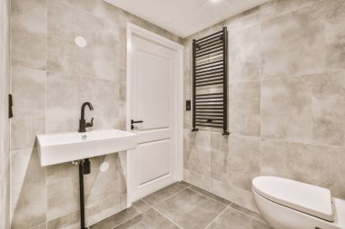 Çağdaş dairenin küçük fayanslı banyosunda lavabo ve duş arasında bulunan sifon tuvaleti