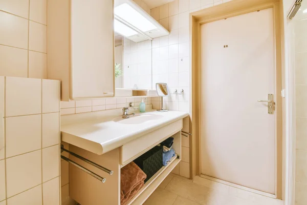 Cupboard with sink and mirror attached to tiled wall near door and drying rack in modern restroom